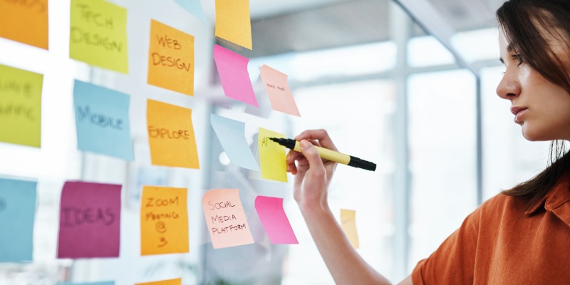 Woman writing information on sticky notes and sticking up on wall